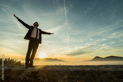 Businessman in elegant suit standing on a wall with his arms spread widely