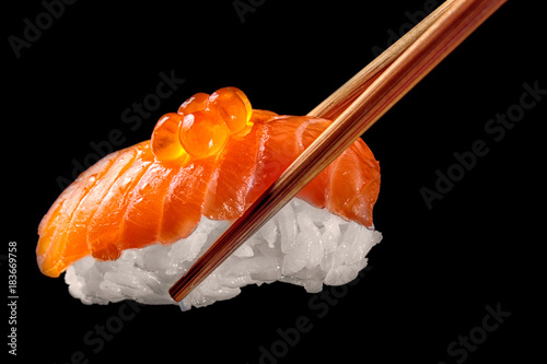 Salmon sushi nigiri in chopsticks isolated on black background.Close up.