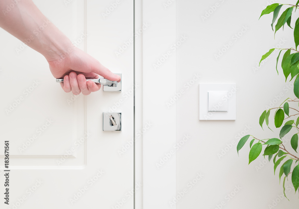 Naklejka premium Male hand holding modern door handle. Close-up elements of the interior of the apartment. White door and lock with key