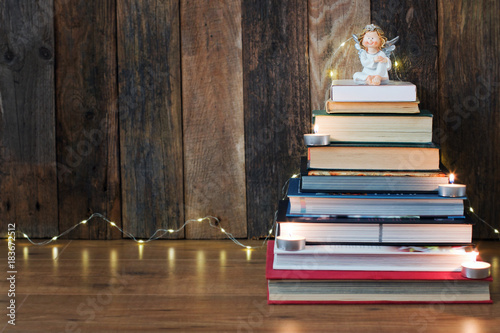 Christmas background with a pile of books, an angel, candles and a fir-tree garland