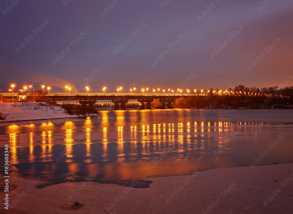Bridge on the River Dnieper in the evening. Lantern light is reflected in the frozen ice, city