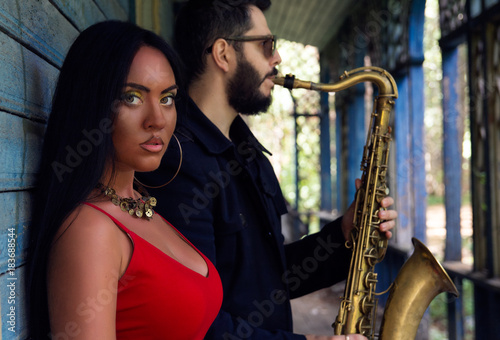 Young beautiful girl singer  with saxophone players on old house background. musical duet 