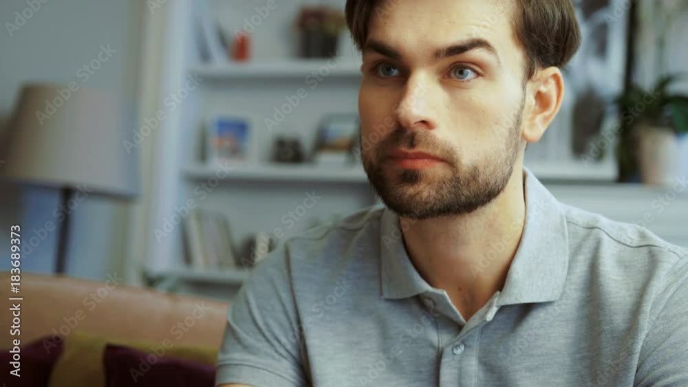 Portrait of young handsome man sitting on the couch and turning on TV with the remote control at home. Close up Portrait of young handsome man sitting on the couch and turning on TV with the remote control at home. Close up
