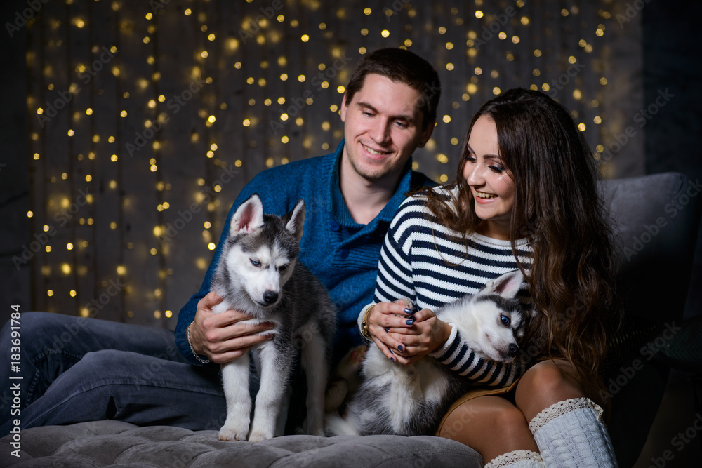 Beautiful young couple in the New Year atmosphere with puppies of the Husky