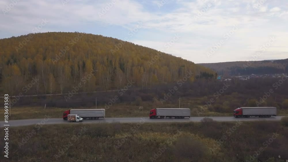 Freight trucks and cars moving on suburban road on background autumn forest Freight trucks and cars moving on suburban road on background autumn forest
