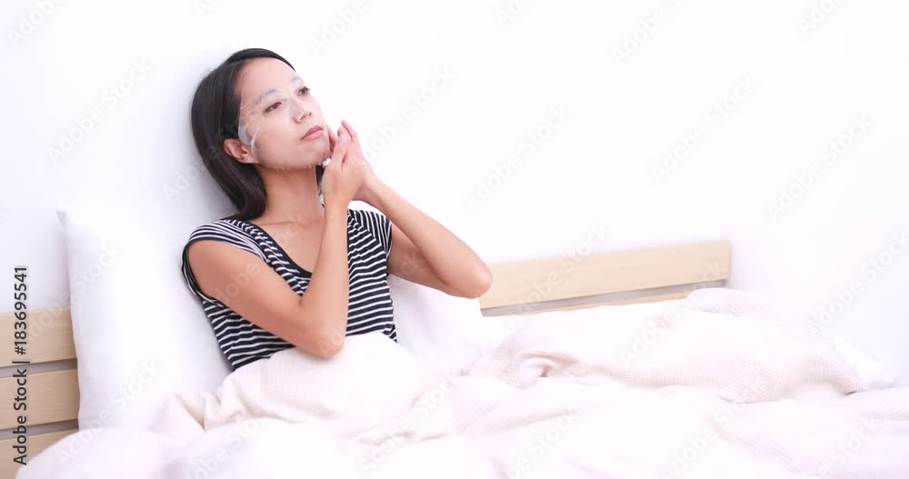 Woman apply paper mask on her face and sitting on bed Woman apply paper mask on her face and sitting on bed