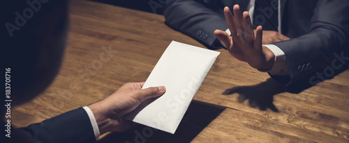 Businessman rejecting money in white envelope offered by his partner in the dark, anti bribery concept