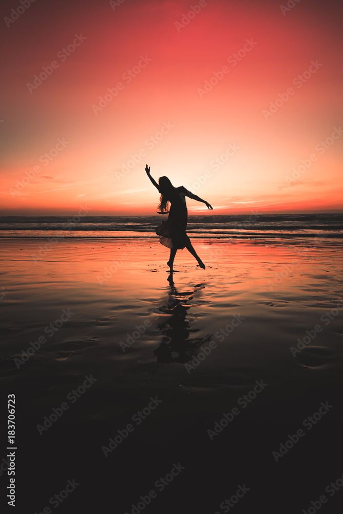 silhouetted girl dancing at sunset on the beach