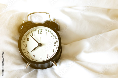 vintage black alarm clock at 8:00 am on a soft white bed.