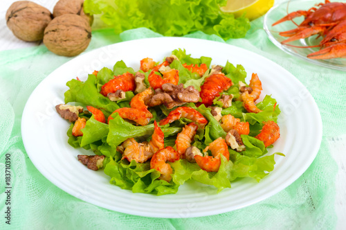 Light dietary spicy salad of lettuce, seafood (crawfish, shrimp) and walnuts on a white wooden background. Proper nutrition