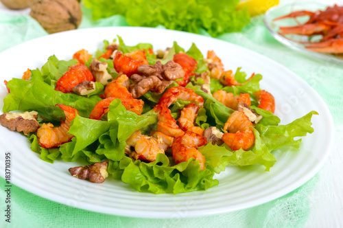 Light dietary spicy salad of lettuce, seafood (crawfish, shrimp) and walnuts on a white wooden background. Proper nutrition