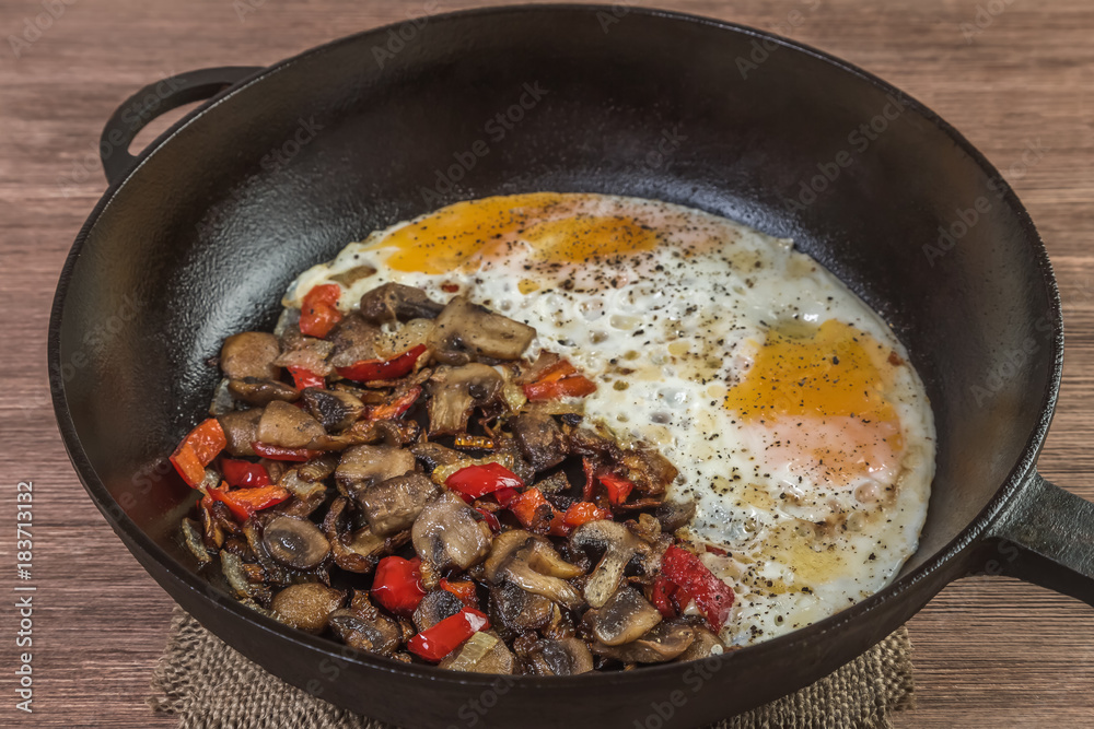 Fried eggs with mushrooms, onions and red pepper in a frying pan. Home-cooked food. Fried eggs with mushrooms, onions and red pepper in a frying pan. Home-cooked food.