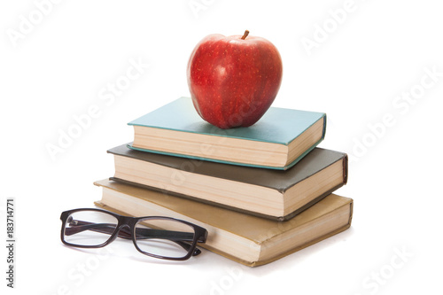 Three old books, glasses and a red apple on a white background