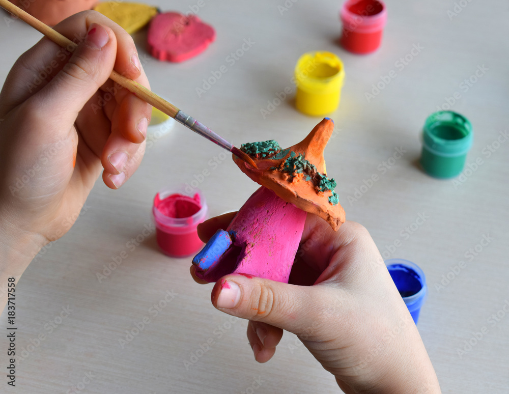 Making toys, paints a pottery clay fairytale house with gouache. Indoors creative leisure for