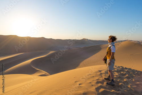 Tourist standing on sand dunes and looking at view in Sossusvlei, Namib desert, travel destination in Namibia, Africa. Concept of adventure and traveling people.