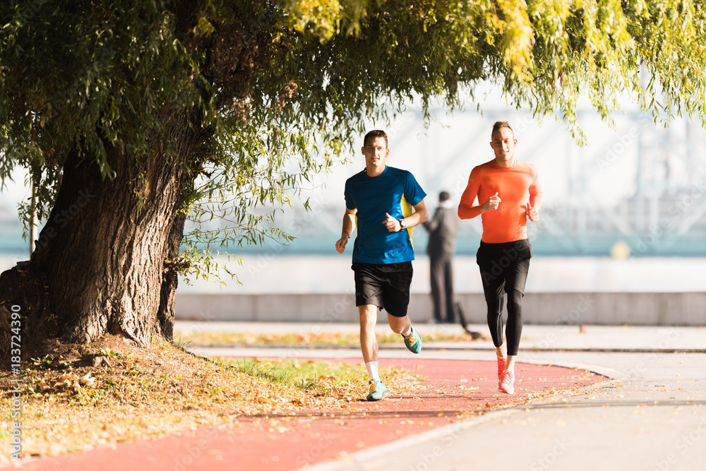 Handsome young men wearing sportswear and running at quay during autumn