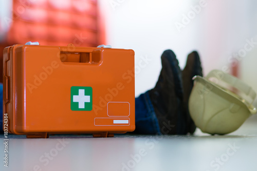 Obraz na płótnie Man lying on the ground after a work accident and a first aid kit stands next to