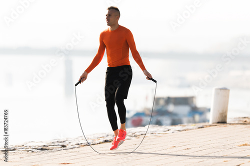 Canvas Print Handsome young man wearing sportswear and  skipping rope at quay during autumn