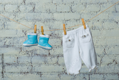 Children's boots and pantyhose dry on a rope against a white brick wall.
