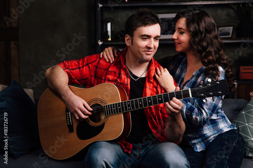 couple is sitting on the couch with a guitar. Long hair of a brunette with an acoustic guitar.