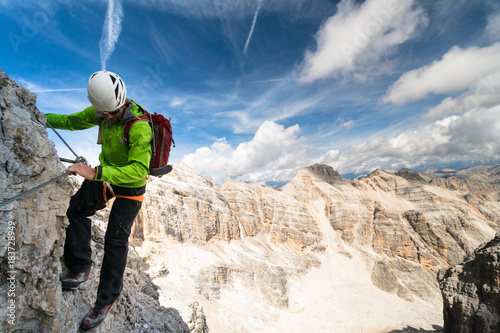 male mountain climber in a green jacket on an exposed Via Ferrata in the Dolomites in Italy with a great view of the surrounding landscape