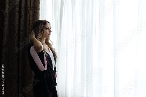 Beautiful young woman dressed in a robe standing near a window in a hotel.