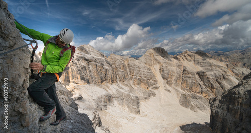 male mountain climber in a green jacket on an exposed Via Ferrata in the Dolomites in Italy with a great view of the surrounding landscape