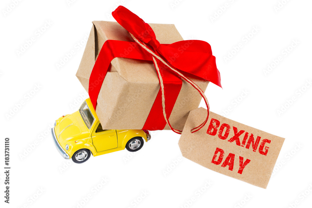 BOXING DAY concept. Yellow retro toy car delivering gifts box with tag with text BOXING DAY on white background