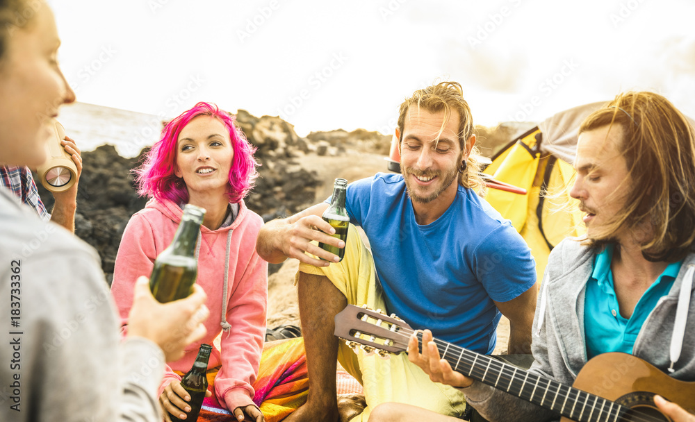 Hipster friends having fun together at beach camping party - Friendship travel concept with young people travelers playing guitar and drinking bottled beer at summer surf camp - Warm bright filter Hipster friends having fun together at beach camping party - Friendship travel concept with young people travelers playing guitar and drinking bottled beer at summer surf camp - Warm bright filter