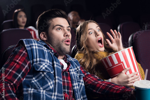 young shocked couple with popcorn watching movie in cinema