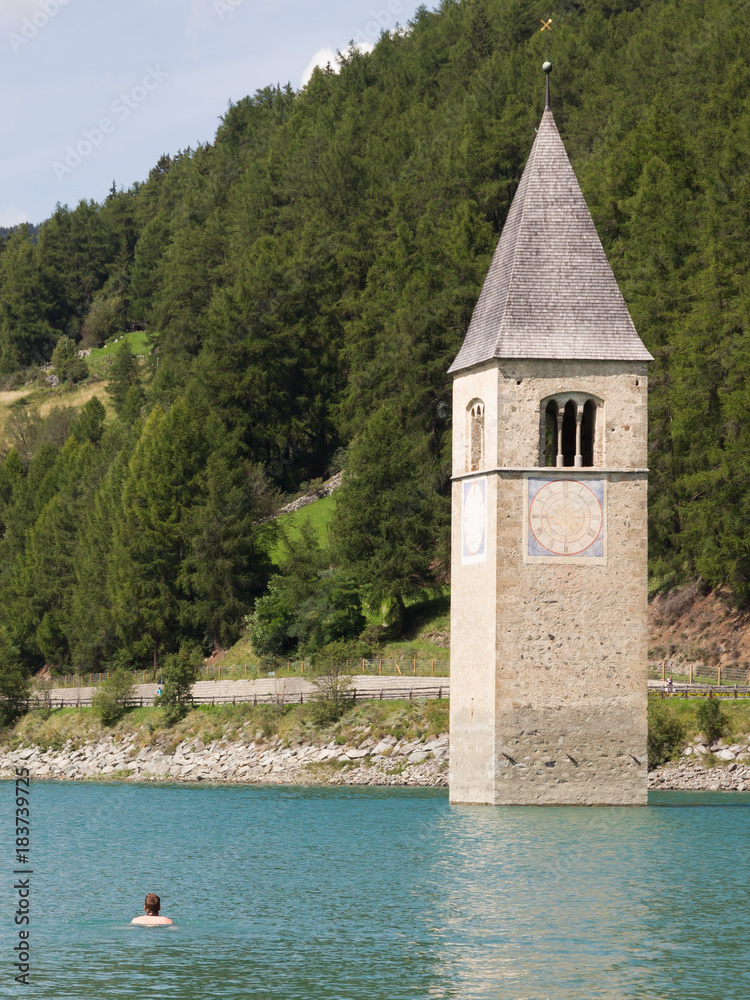 Submerged tower of reschensee church, man swimming next to it
