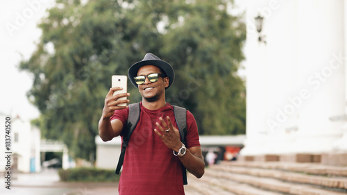 Fototapeta Naklejka Na Ścianę i Meble -  Happy african american tourist man having online video chat using his smartphone camera while travelling in Europe