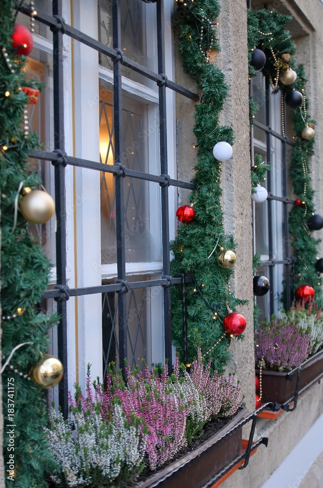 Okna od ulicy udekorowane świątecznie, z girlandami, choinkowymi bombkami i doniczkami z wrzosami