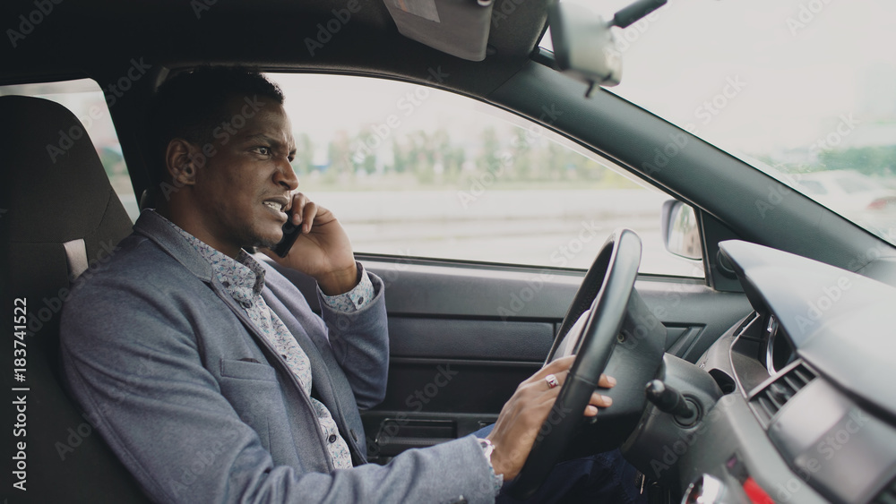 Angry mixed race businessman talking phone while sitting inside his car outdoors Angry mixed race businessman talking phone while sitting inside his car outdoors