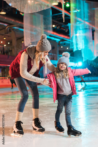 beautiful happy mother and daughter ice skating together on rink