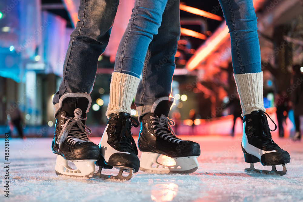 close-up partial view of young couple in skates ice skating on rink - obrazy, fototapety, plakaty 