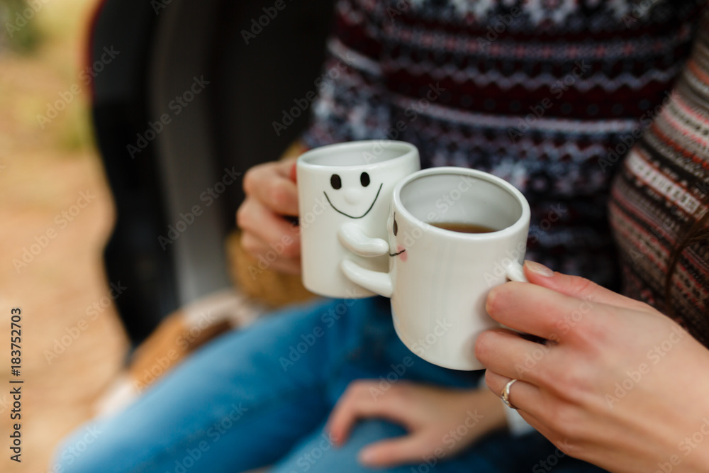 Tourists sit in the car, open the trunk and drinking tea from a thermos. Tea party in the trunk of the car - a couple in love drinking hot tea from a thermos sitting in the trunk of the car. Closeup.