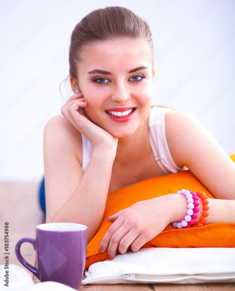 Smiling young woman lying on a white floor with pillow Smiling young woman lying on a white floor with pillow