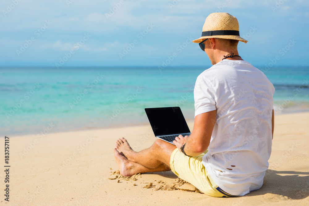 Casual looking guy using laptop on the beach