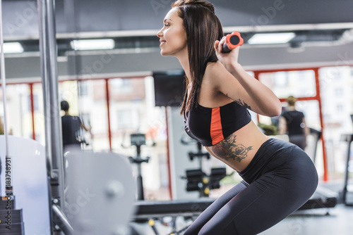side view of attractive young sportive woman doing squats at gym
