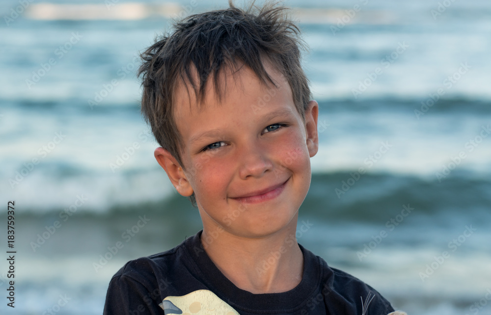 Portrait of a handsome boy with an Eupropean appearance. A sweet sunbathing baby boy smiles tenderly against the backdrop of the sea at sunset. Portrait of a handsome boy with an Eupropean appearance. A sweet sunbathing baby boy smiles tenderly against the backdrop of the sea at sunset.