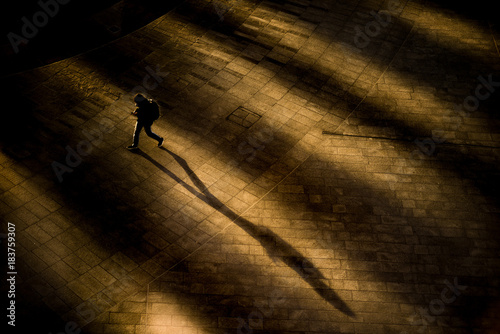 Ragazzo con zaino che cammina all’alba proiettando la sua ombra sul selciato deserto