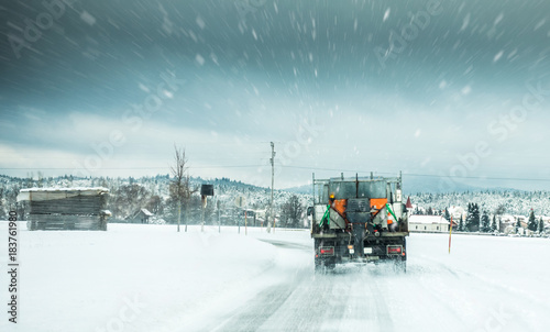 Winter service truck or gritter spreading salt on the road surface to prevent icing in stormy snow winter day. photo