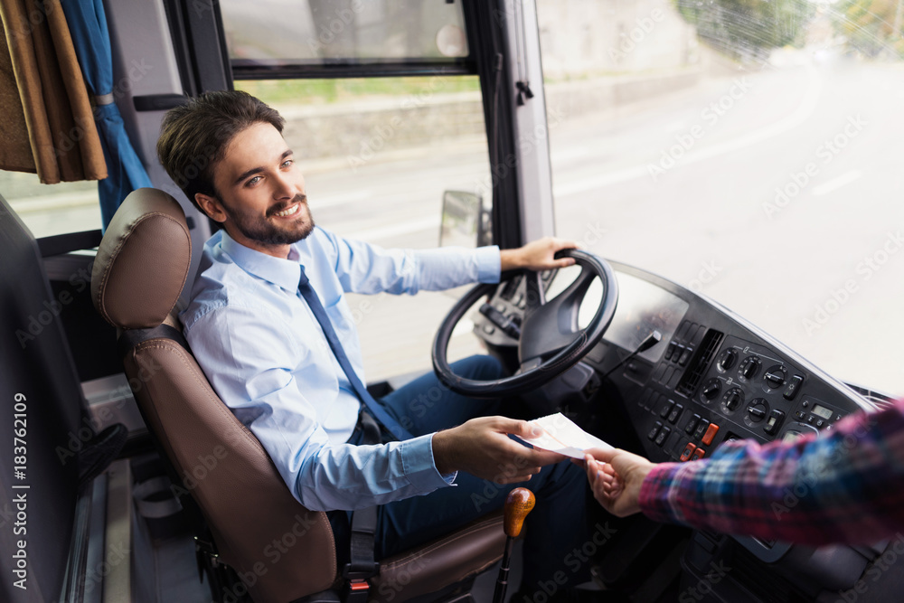 Obraz premium The driver of the tourist bus is smiling and looking at the camera. The passenger gives him a ticket for the bus ride.