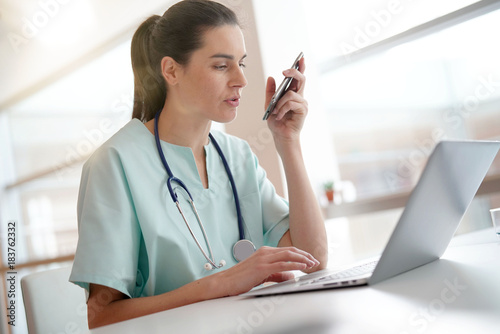 Nurse working on laptop computer and recording on dictaphone photo