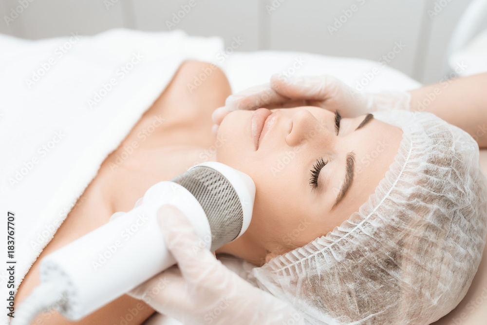 The doctor treats the girl's face with a photoepilator. The girl is lying on the couch in a modern cosmetology salon. The doctor treats the girl's face with a photoepilator. The girl is lying on the couch in a modern cosmetology salon.