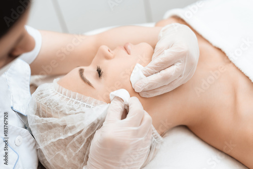 The doctor makes the girl a facial cleansing massage. The girl came to the procedure of laser hair removal.