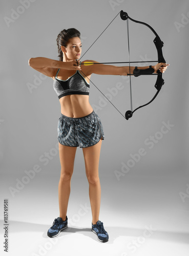 Sporty young woman practicing archery on grey background