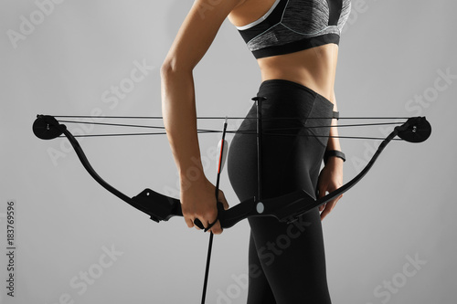 Sporty young woman with bow and arrow for practicing archery on grey background