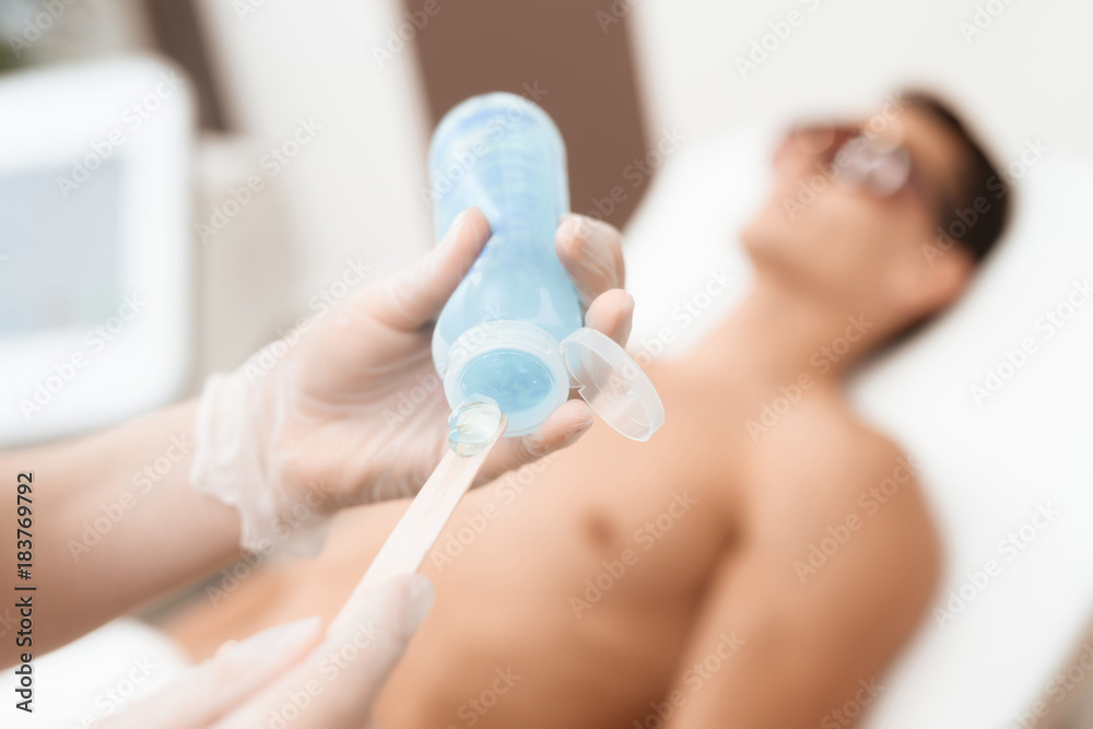 The doctor takes a special gel from the jar for laser hair removal. Against  the backdrop lies the man. Stock Photo | Adobe Stock